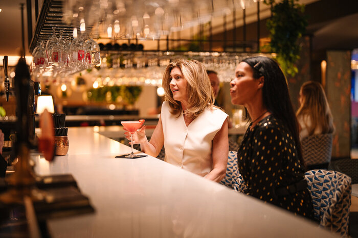 Two ladies with cocktails sat at bar