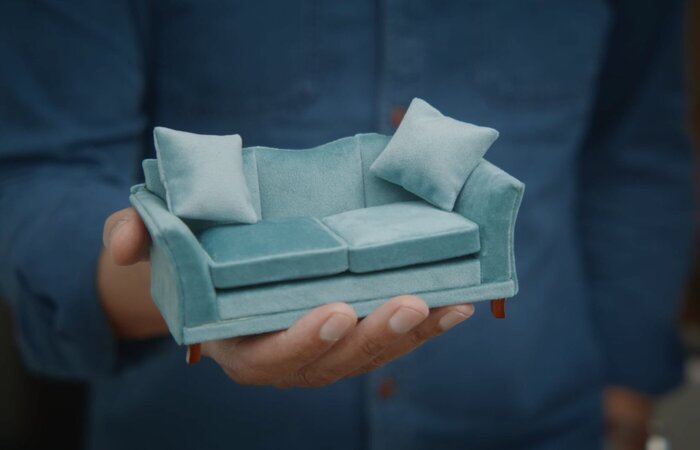 Mans hand holding small blue sofa