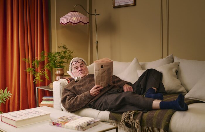 Man laying on sofa reading newspaper