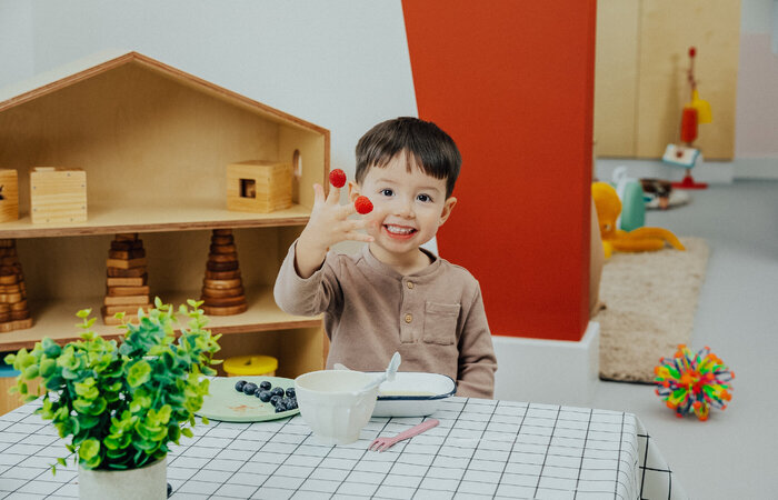 Child smiling with raspberries on fingers
