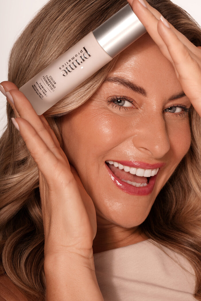Model smiling with foundation bottle
