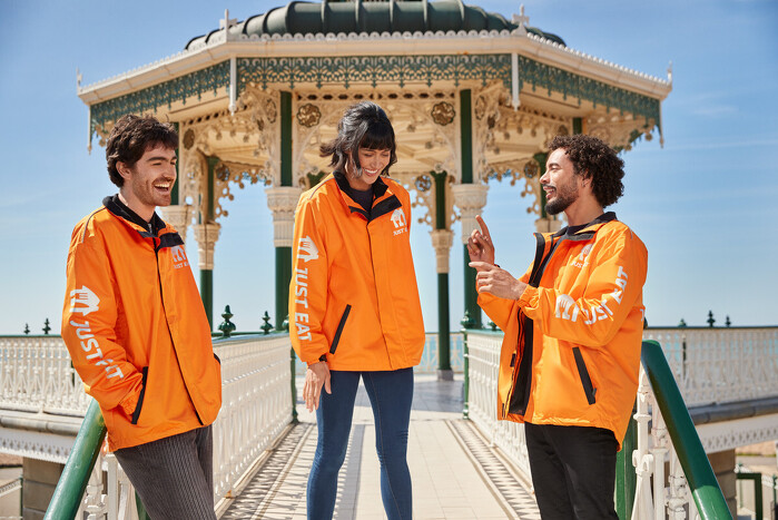 Three models dressed in orange uniforms laughing at band stand by the sea