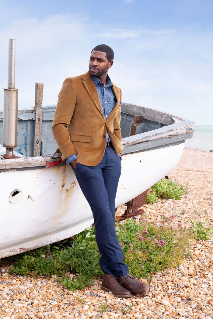 Male model in formal wear leaning against boat at the beach