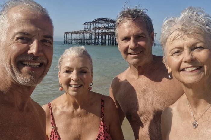 Four friends smiling at the beach in front of West pier