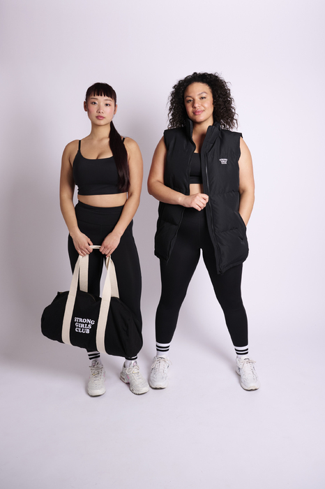 Two female models wearing fitness wear holding a bag