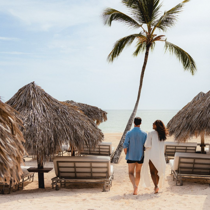 Couple walking arm in arm towards the sea on a beautiful beach with palm tree