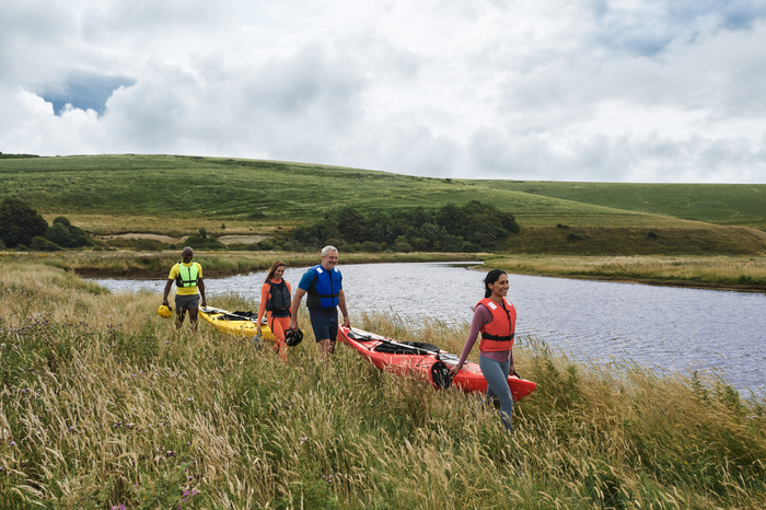 Four models carrying canoes beside a lake smiling and happy