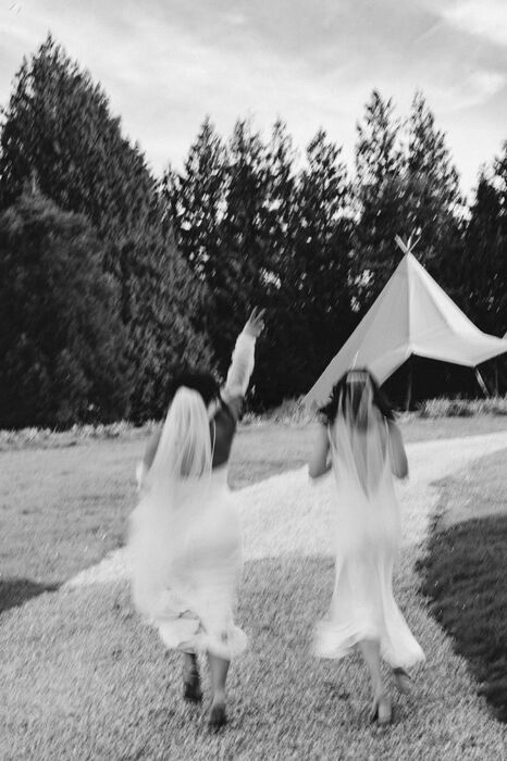 Two brides running hand in hand away from camera